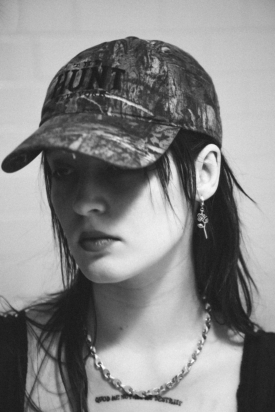 Black and white photo of a person wearing a camouflage cap and necklace.