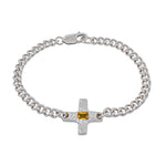 A silver chain bracelet with a textured cross charm featuring a small rectangular yellow gemstone, shown on a plain white background.
