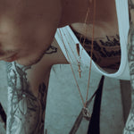 Close-up of a person wearing multiple gold necklaces with tattoos on their arm.