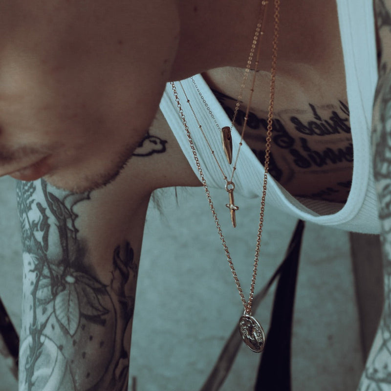 Close-up of a person wearing multiple gold necklaces with tattoos on their arm.