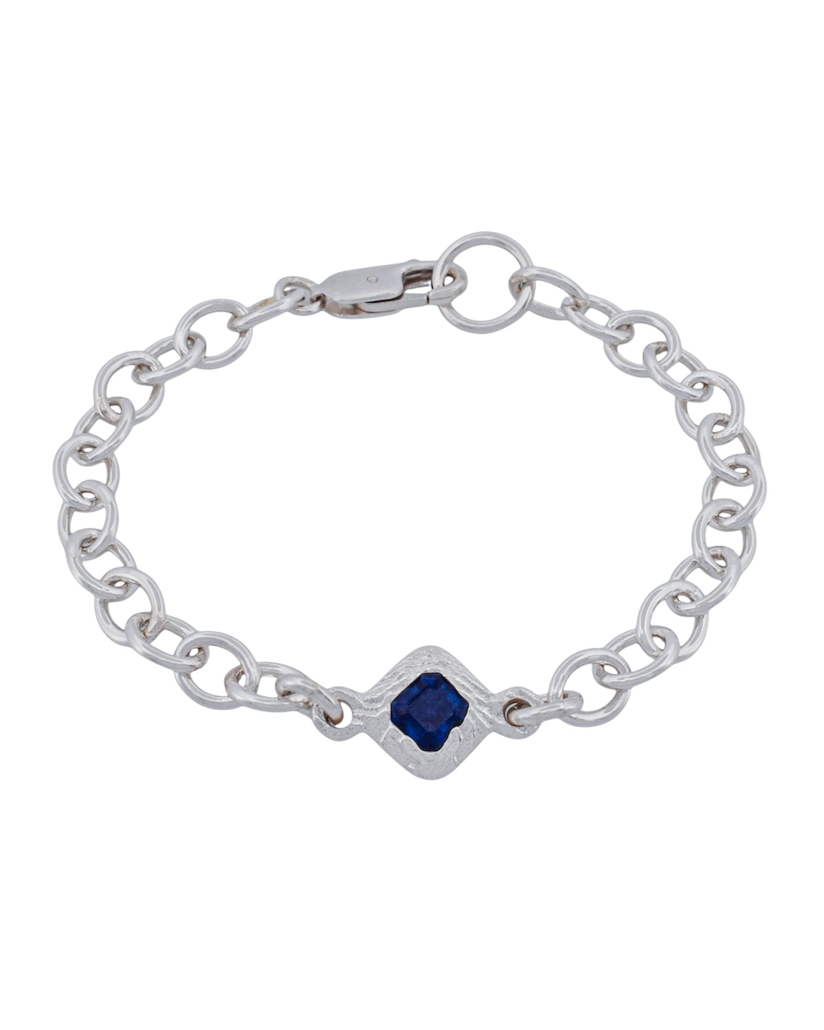 A silver chain bracelet featuring a central diamond-shaped bezel set with a deep blue square gemstone, photographed on a solid white background.