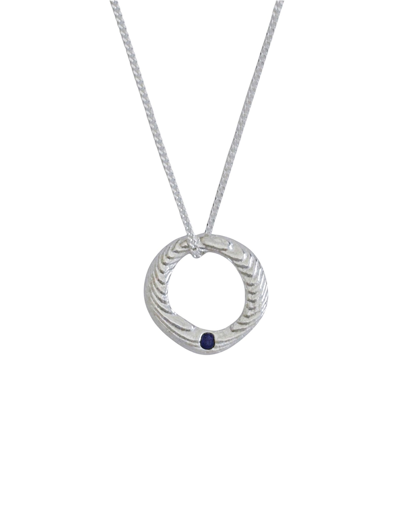 A silver pendant necklace featuring a textured circular ring with a small dark blue gemstone accent, suspended from a delicate silver chain against a plain white background.