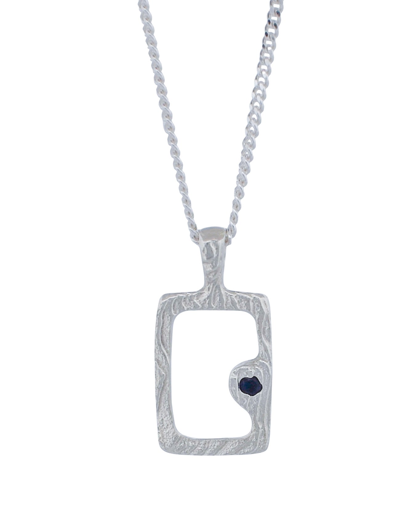A silver pendant necklace featuring a textured rectangular frame with a small dark heart-shaped stone set on the lower right side, suspended from a silver chain against a plain white background.