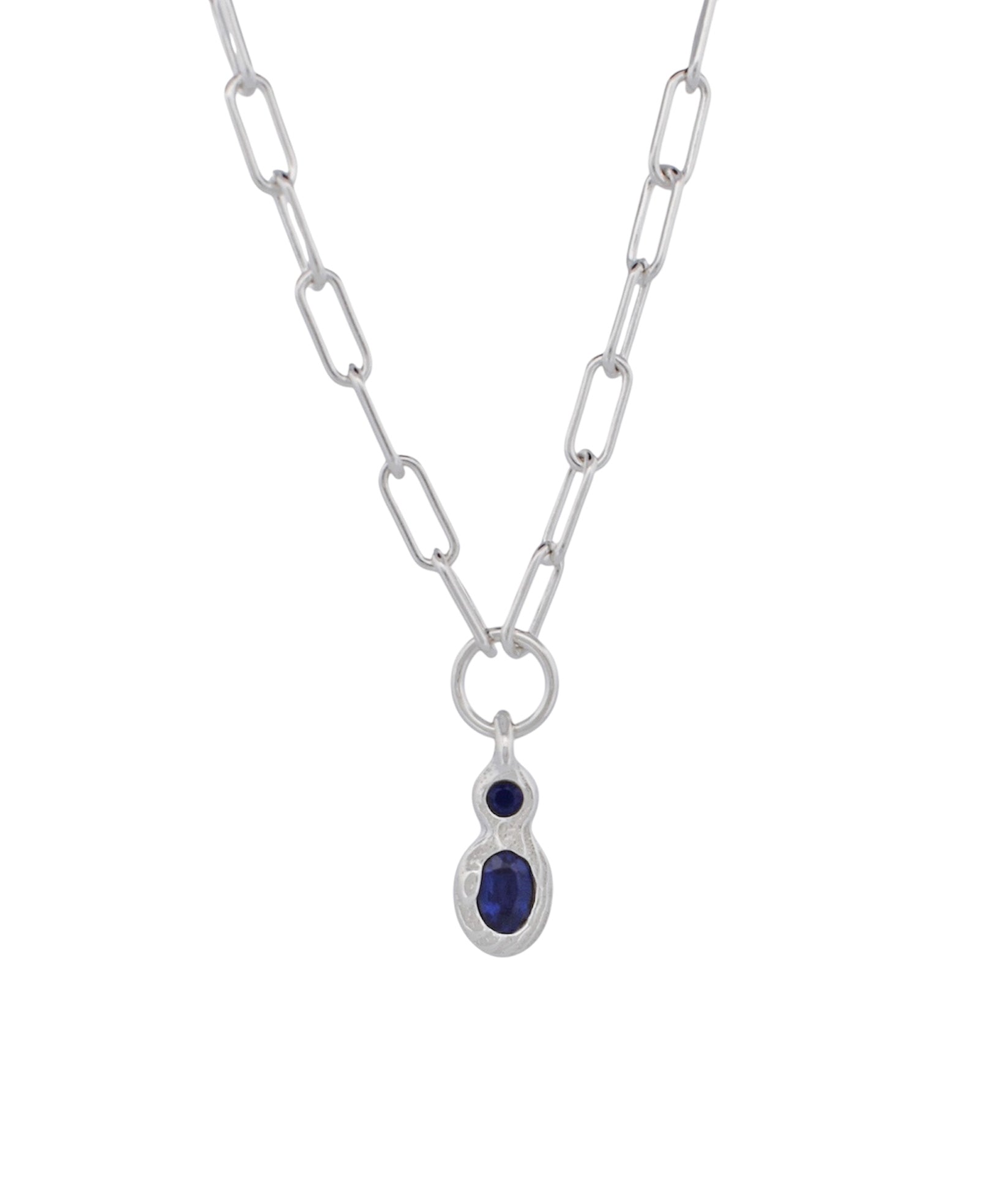 A silver paperclip chain necklace with a teardrop-shaped silver pendant featuring a small round dark blue gemstone above a larger oval dark blue gemstone, set against a plain white background.