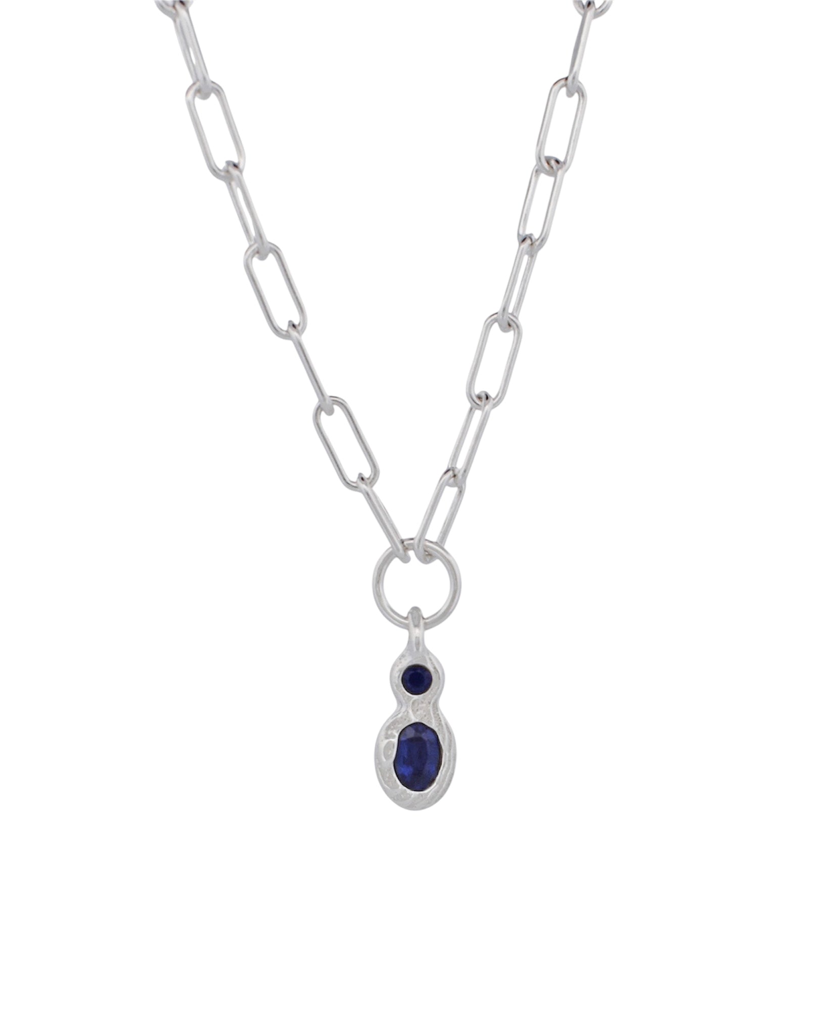 A silver paperclip chain necklace with a teardrop-shaped silver pendant featuring a small round dark blue gemstone above a larger oval dark blue gemstone, set against a plain white background.