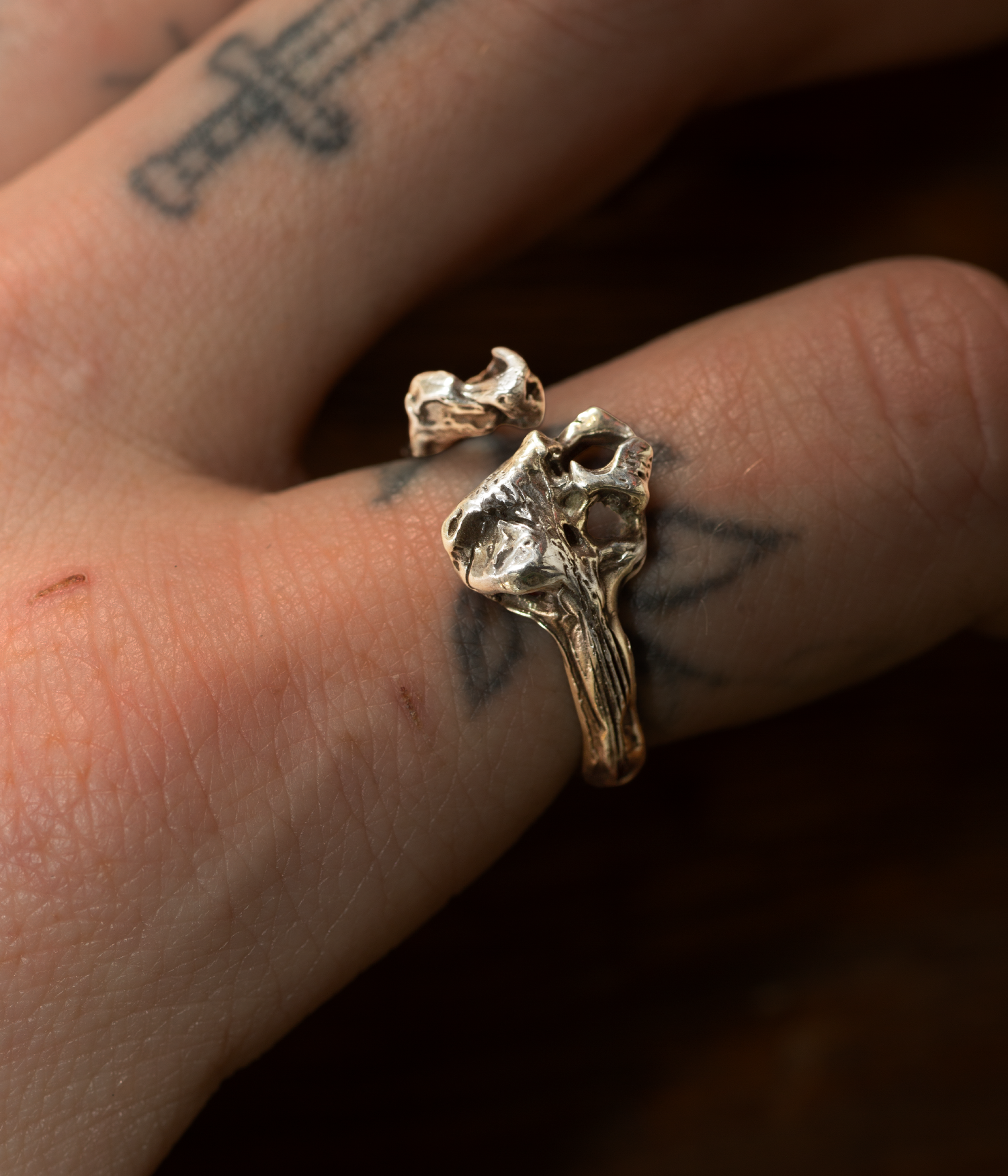 Gold ring with a unique design worn on a finger with tattoos.