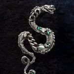 Silver snake-shaped brooch with green and clear gemstones on a black background