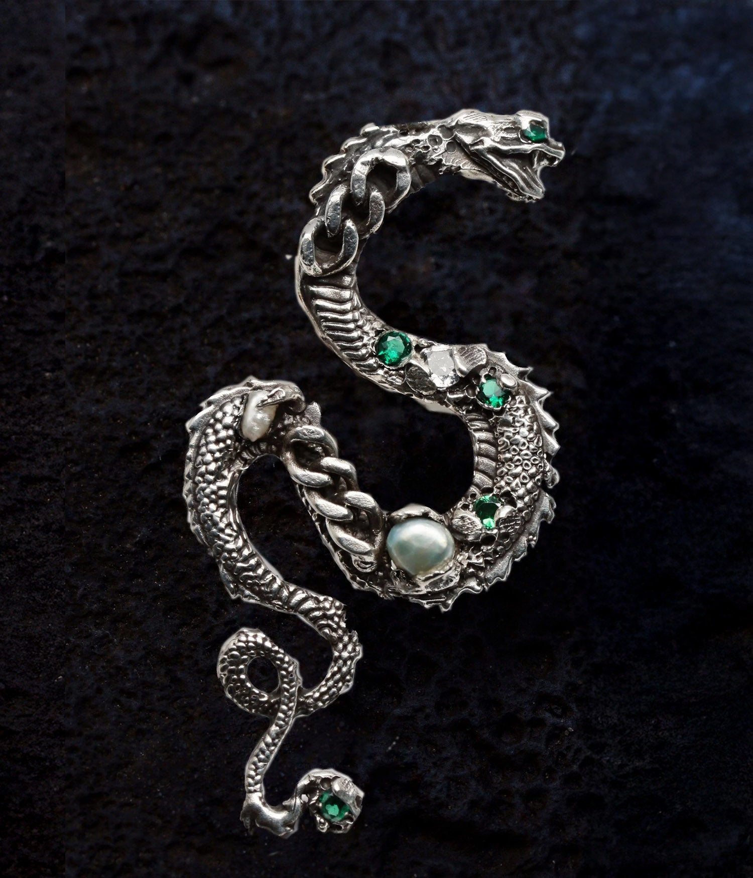 Silver snake-shaped brooch with green and clear gemstones on a black background