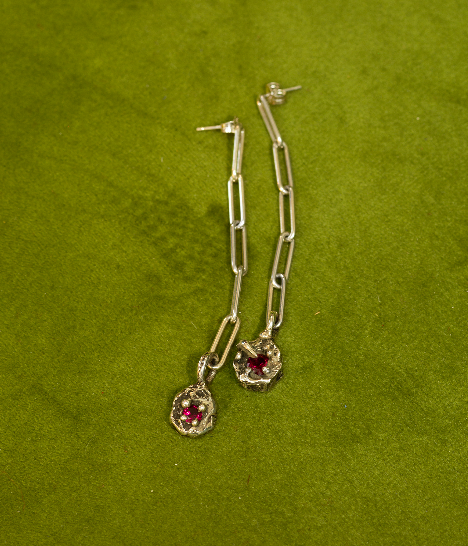 Silver chain earrings with red gemstones on a green background