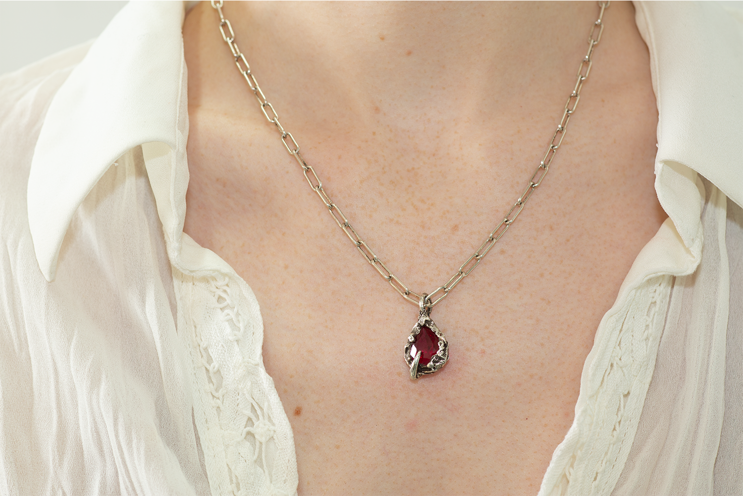 Necklace with a red gemstone pendant worn by a person in a white shirt.