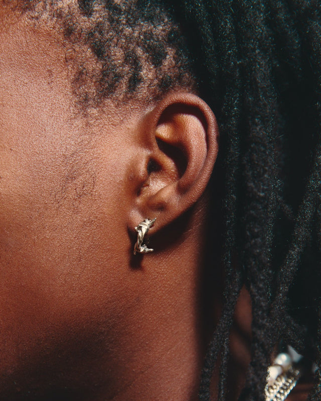 Close-up of an ear with a gold earring and braided hair.