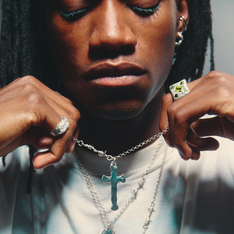 Person wearing a necklace with a cross pendant, close-up of face and hands.