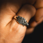 Hand wearing a silver ring with a unique design on a dark background