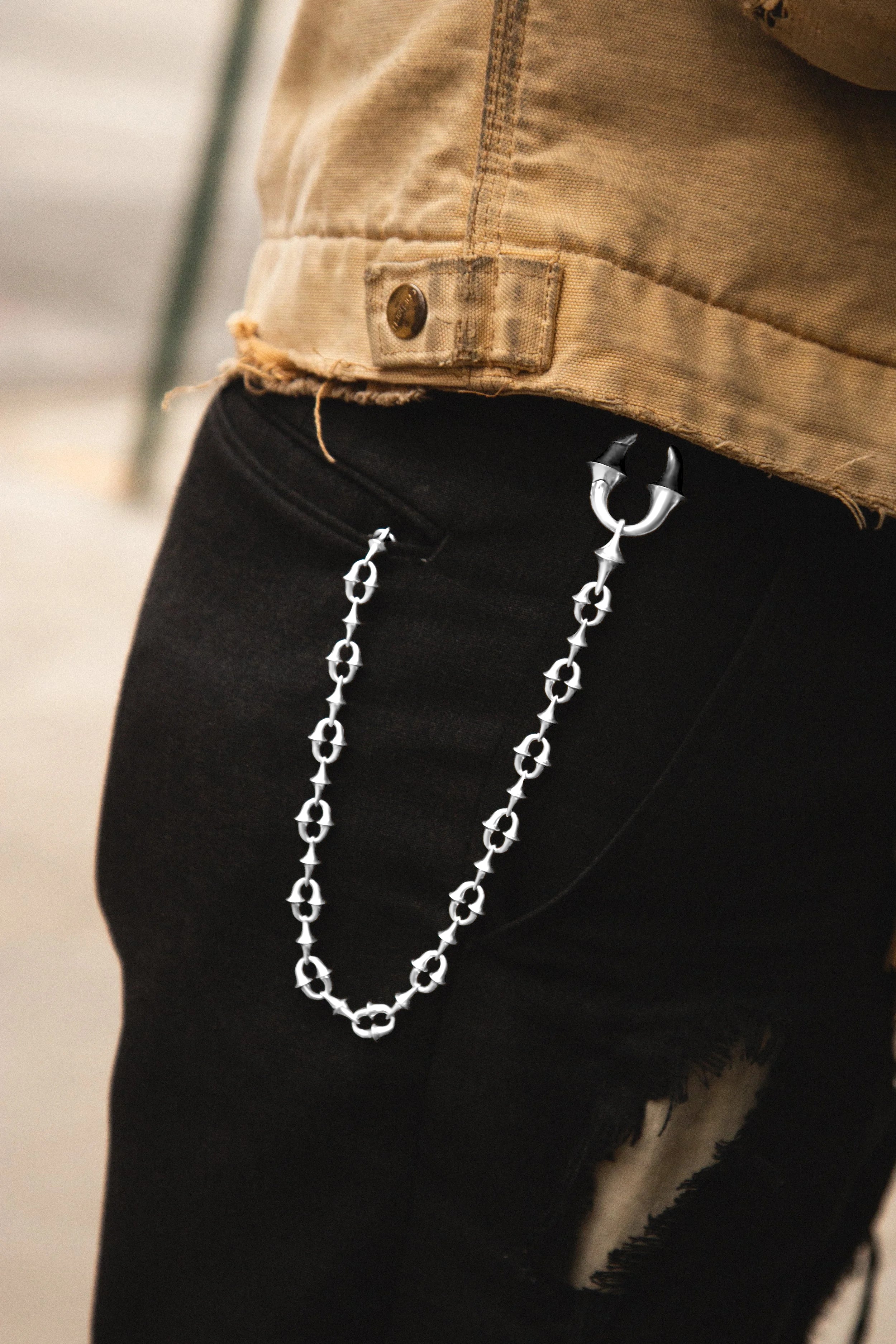 Silver chain hanging from a pocket on black pants with a blurred background