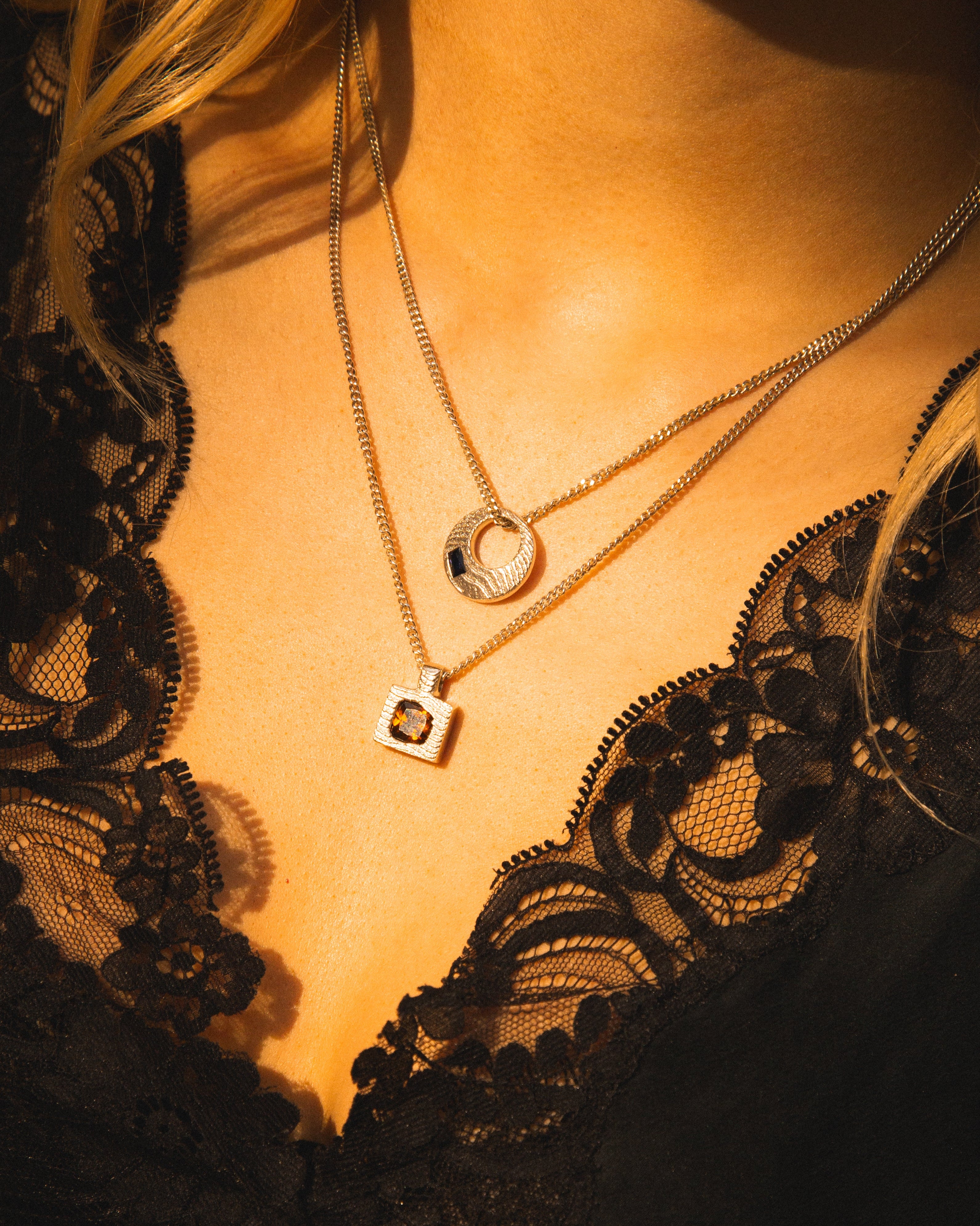 Close-up of a person wearing two necklaces with a black lace garment.