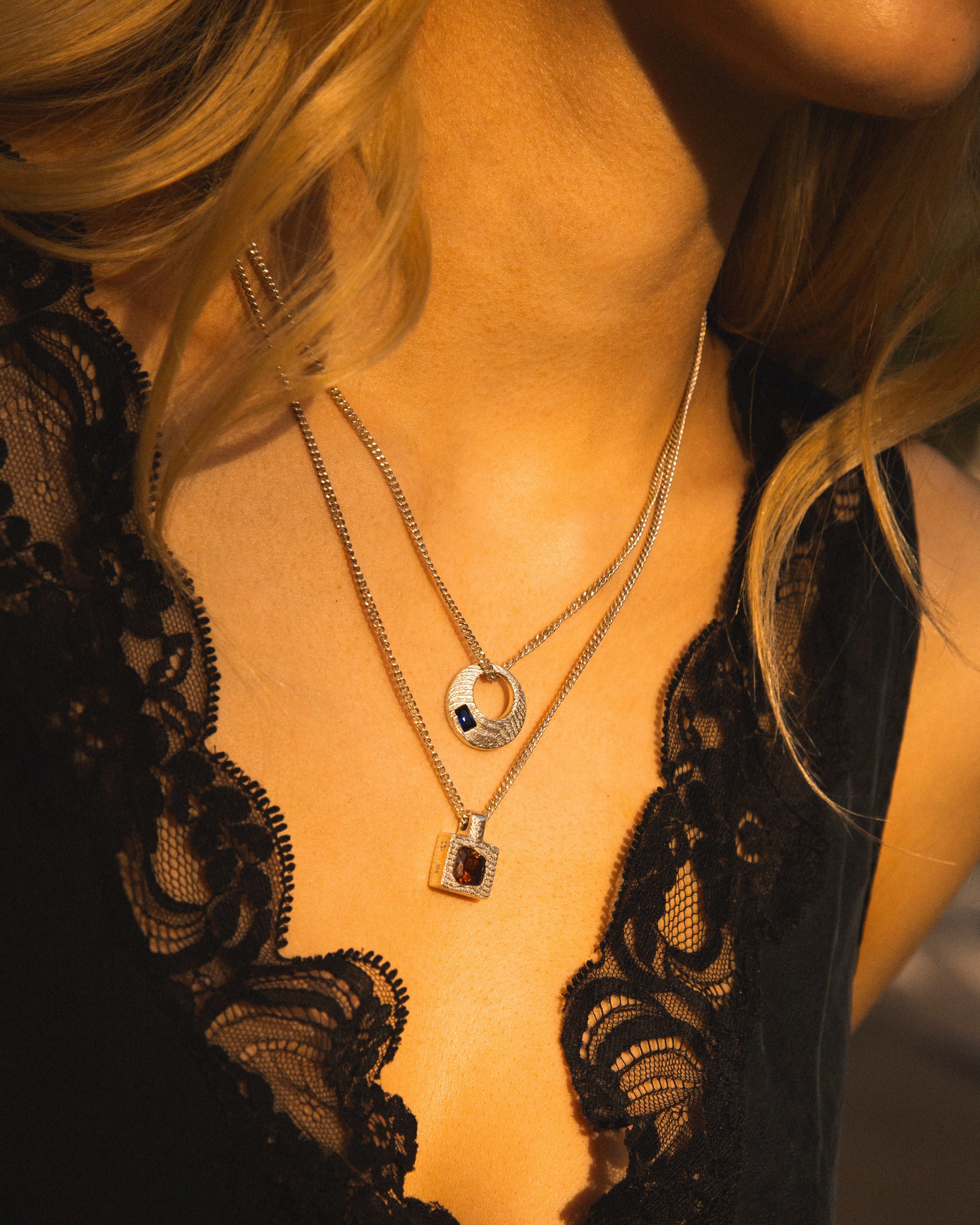 Close-up of a person wearing a black lace top with two necklaces.