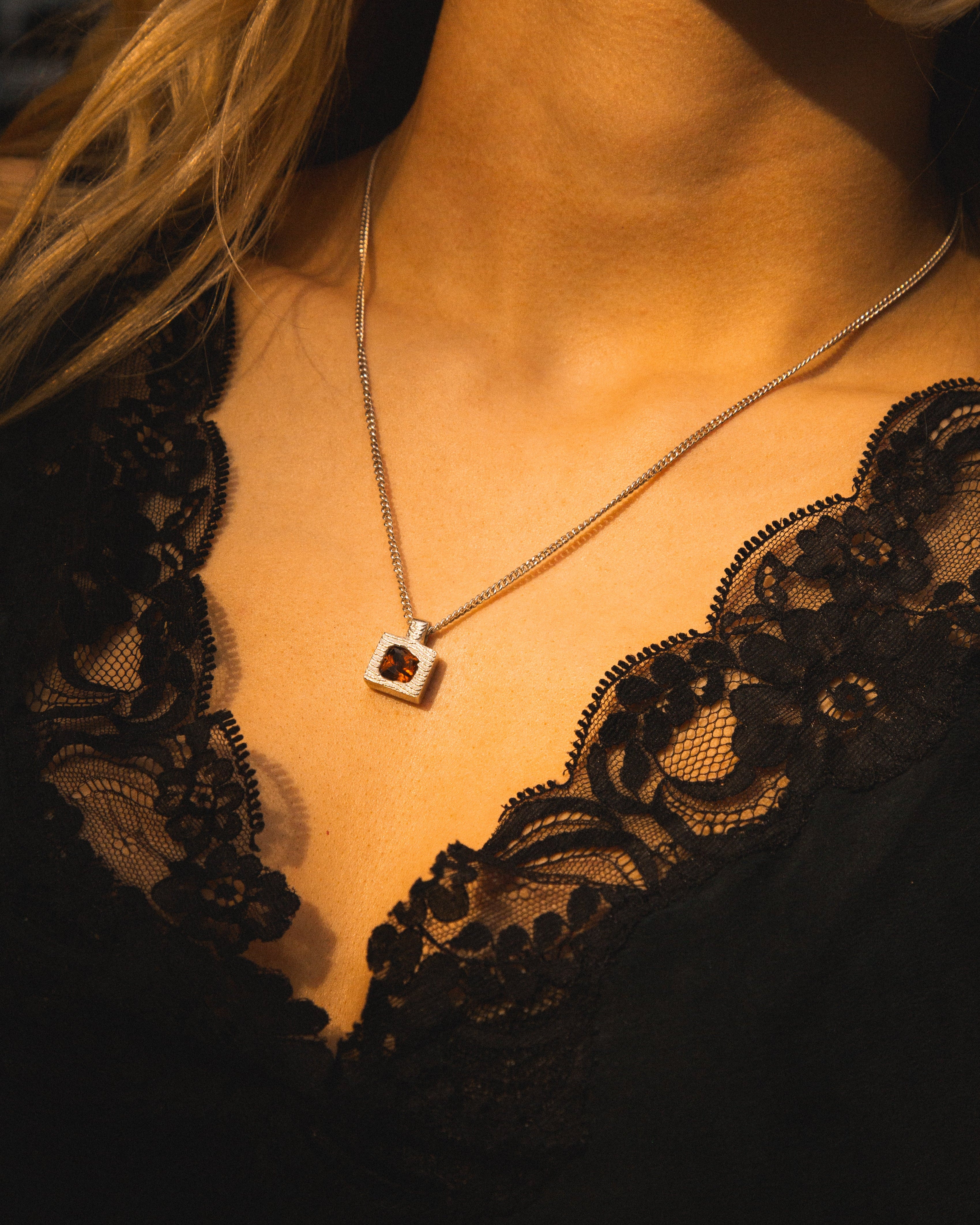 Necklace with a pendant worn by a person in a black lace garment.