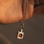 Necklace with a pendant featuring a amber stone held by a hand against a neutral background