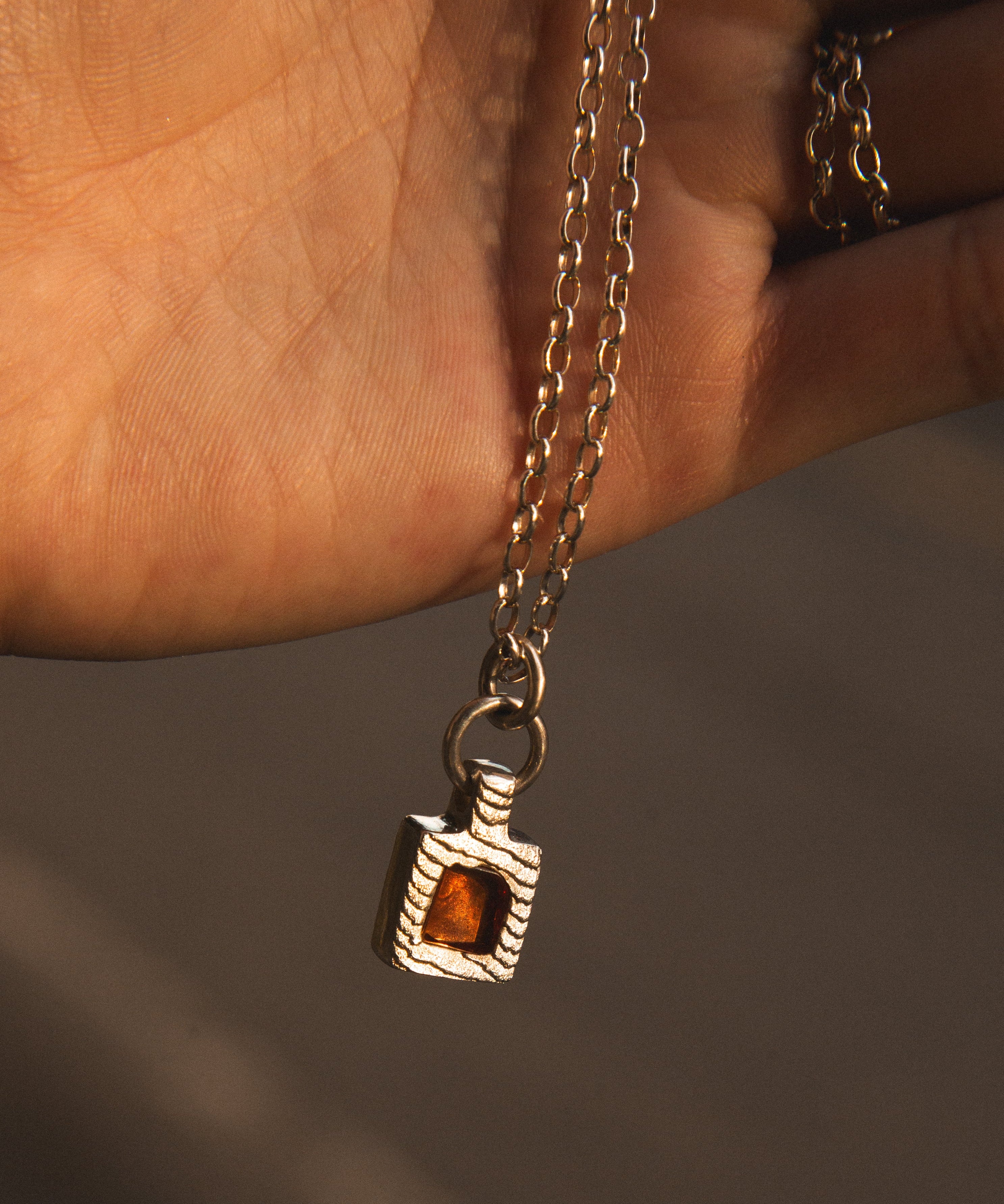 Necklace with a pendant featuring a amber stone held by a hand against a neutral background