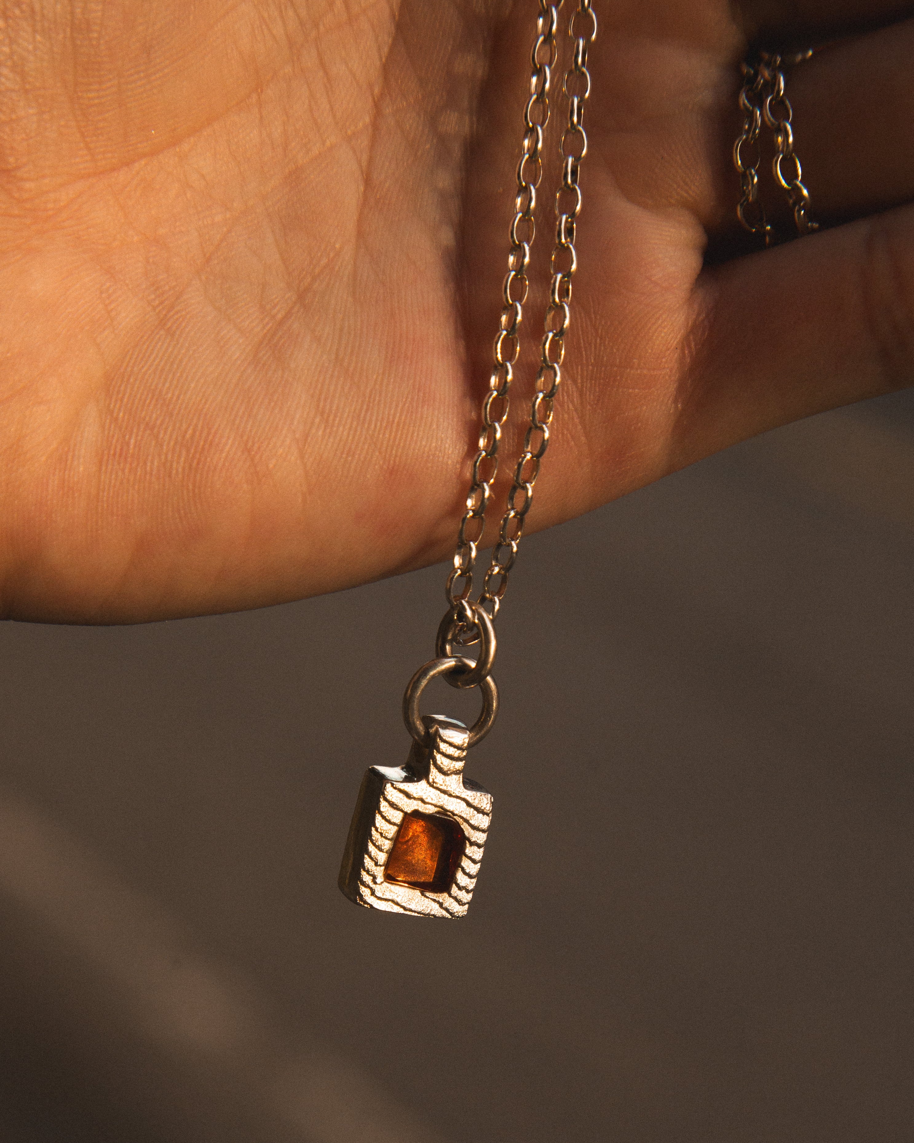 Necklace with a pendant featuring a amber stone held by a hand against a neutral background