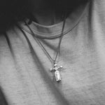 Person wearing a necklace with a cross pendant on a plain background