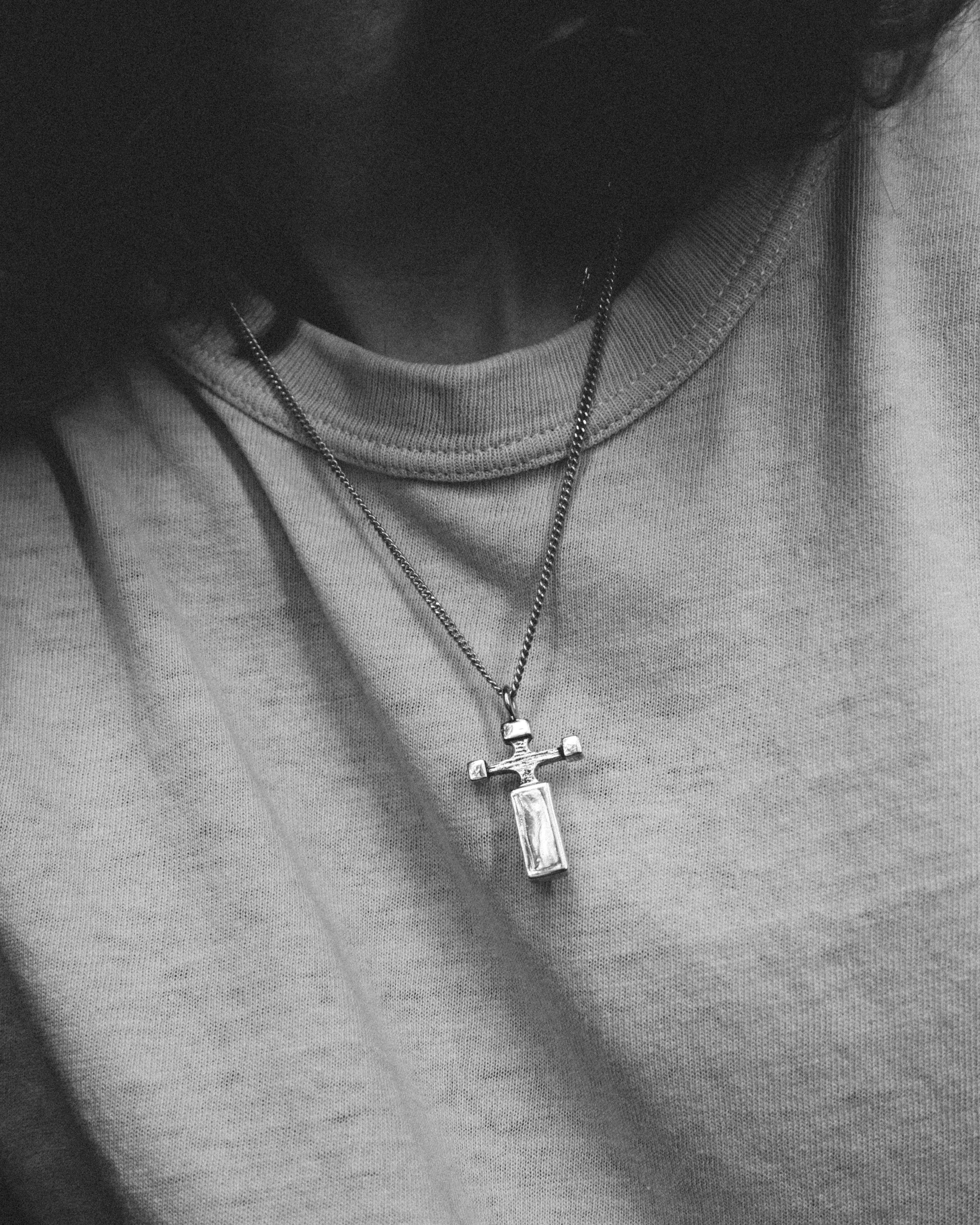 Person wearing a necklace with a cross pendant on a plain background