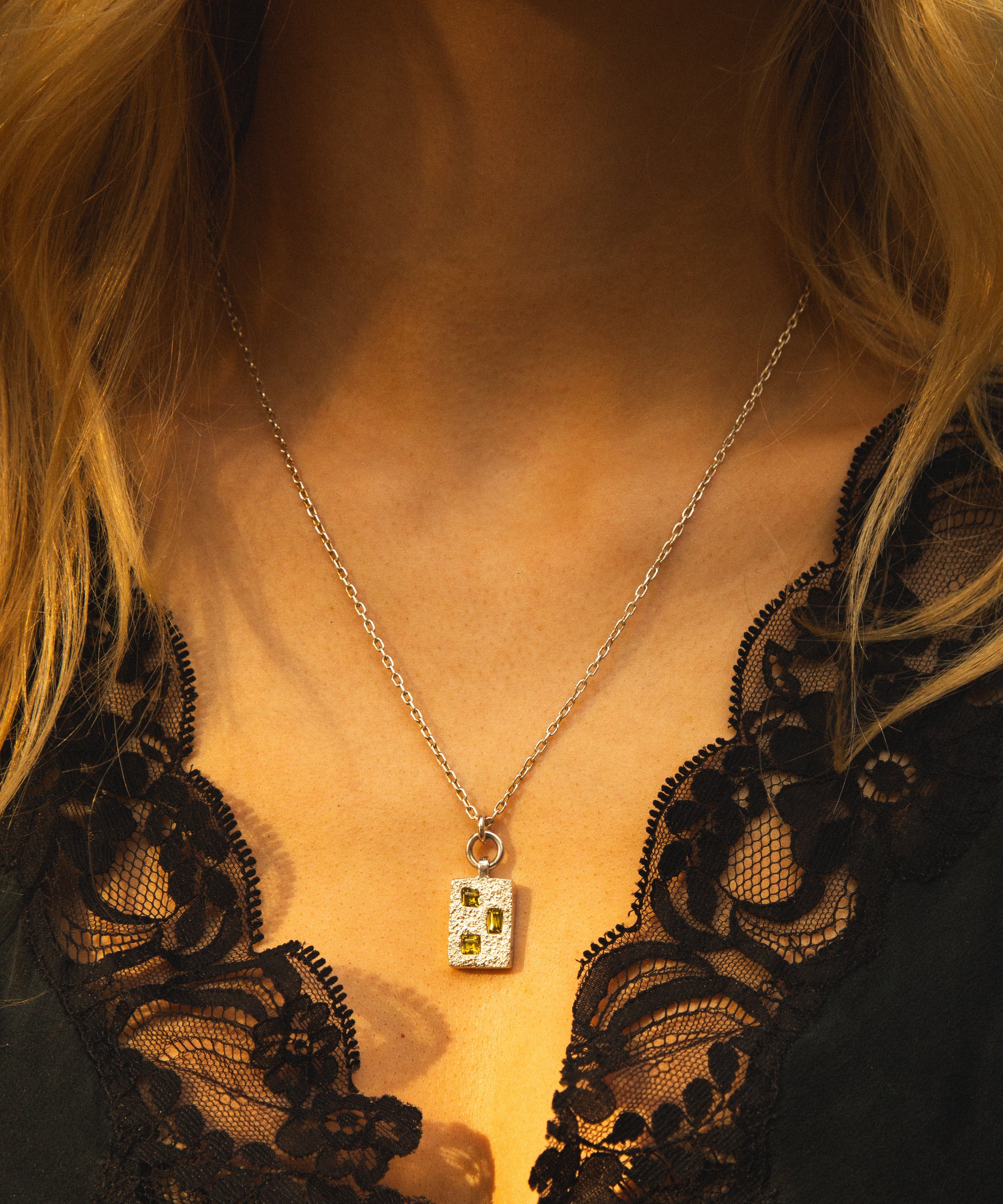 Necklace with a pendant worn by a person in a black lace garment.