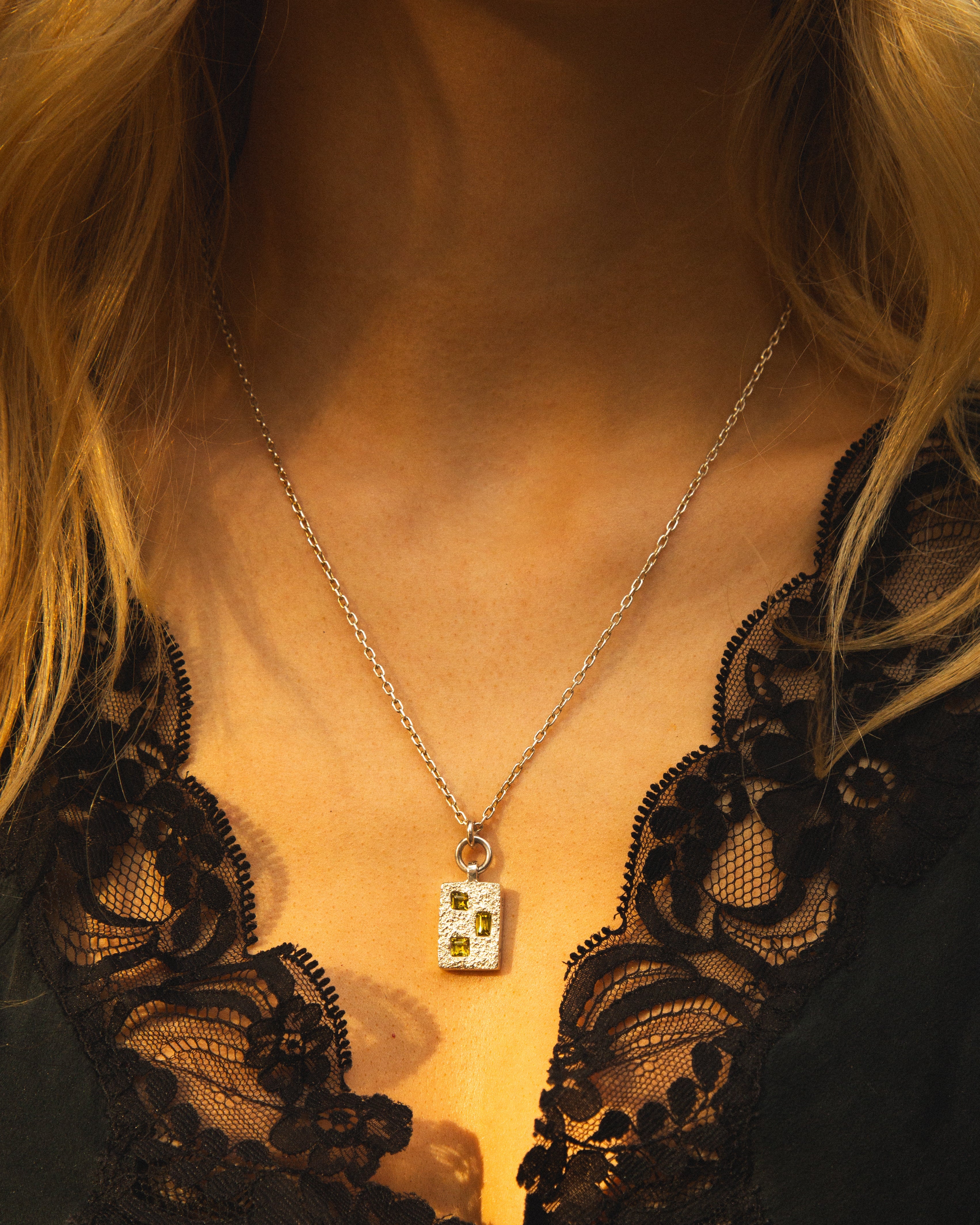Necklace with a pendant worn by a person in a black lace garment.