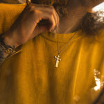 Person wearing a yellow shirt with a necklace featuring a cross pendant.