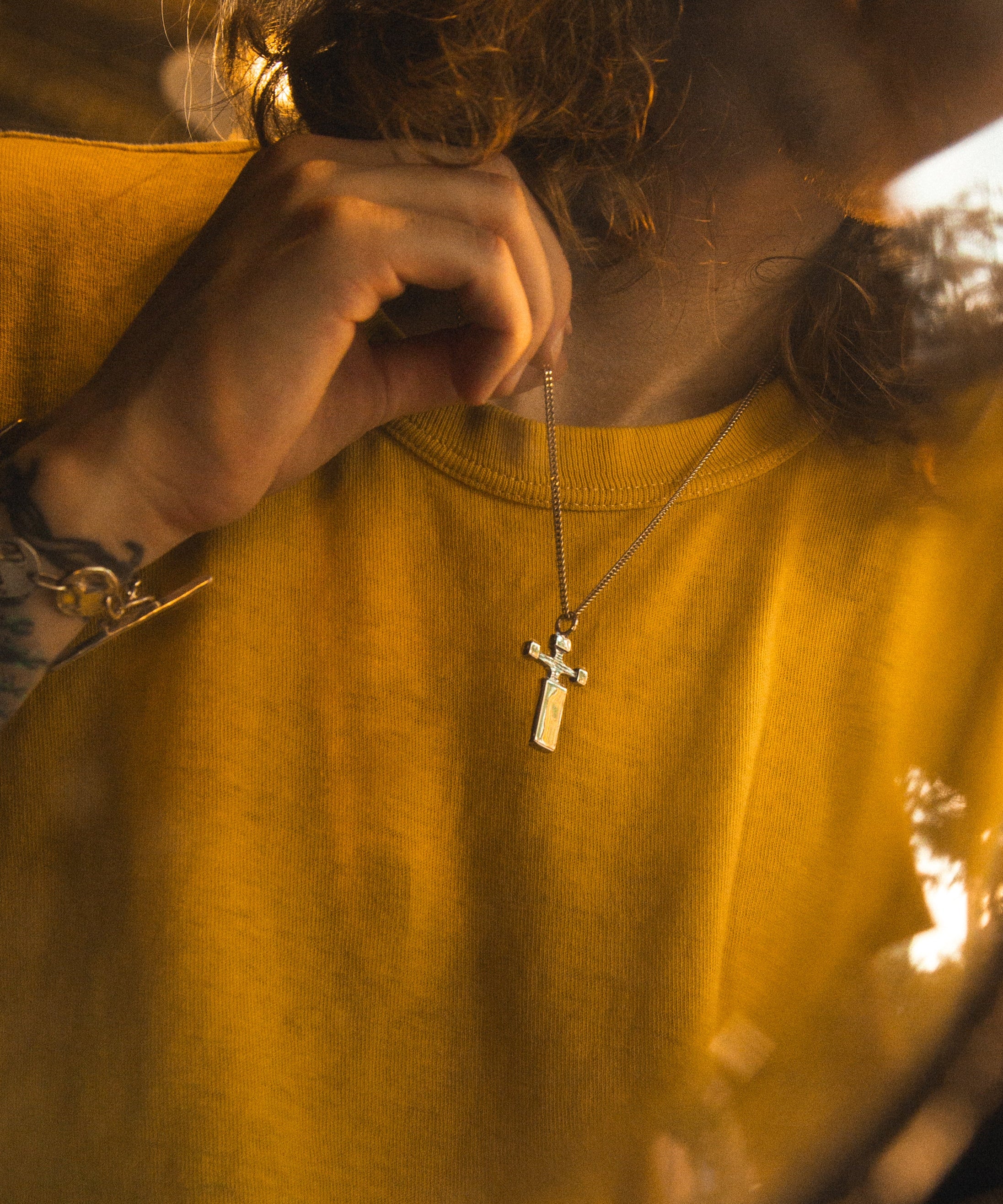 Person wearing a yellow shirt with a necklace featuring a cross pendant.