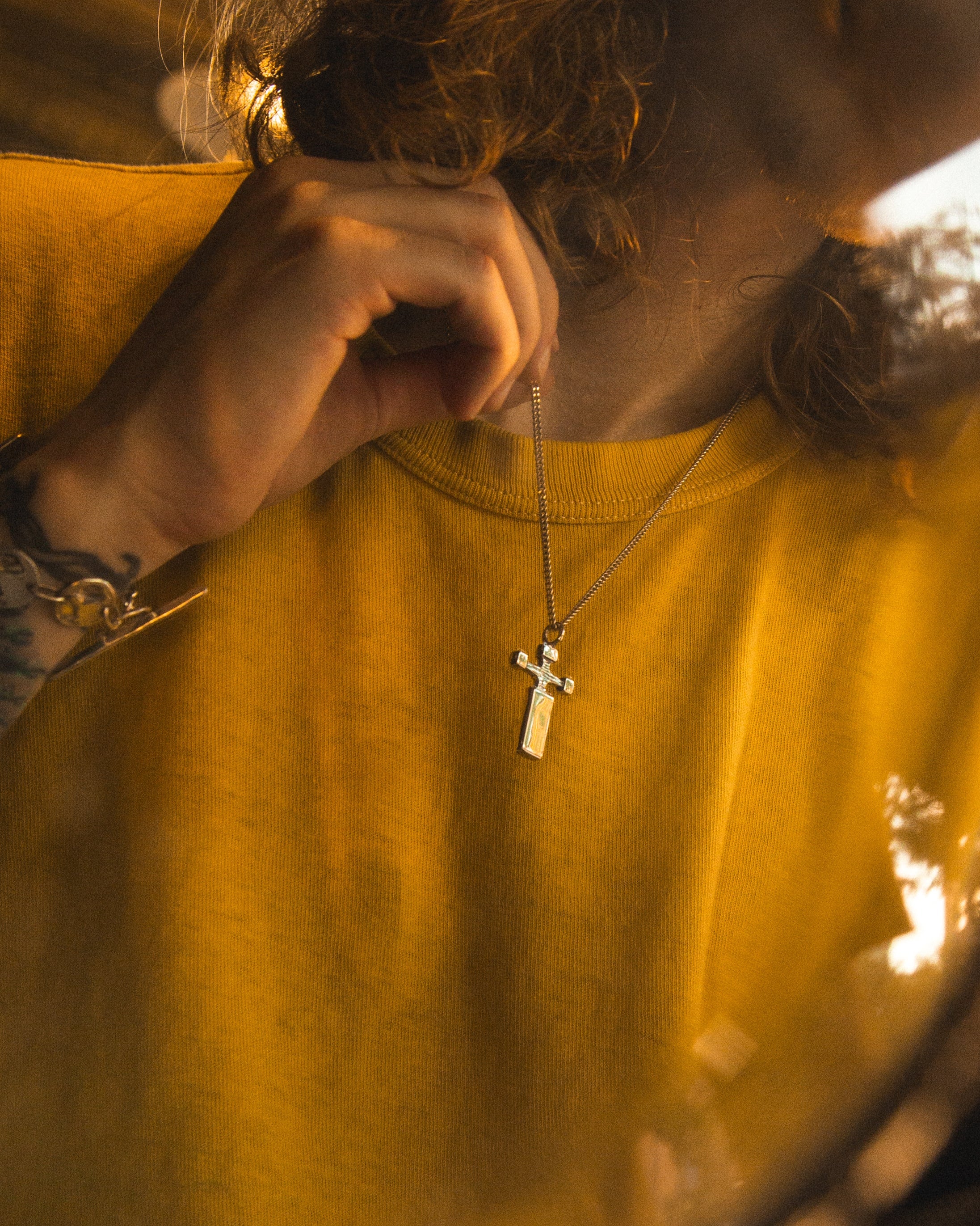 Person wearing a yellow shirt with a necklace featuring a cross pendant.