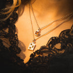 Close-up of a person wearing a gold necklace with a pendant, set against a dark lace garment.