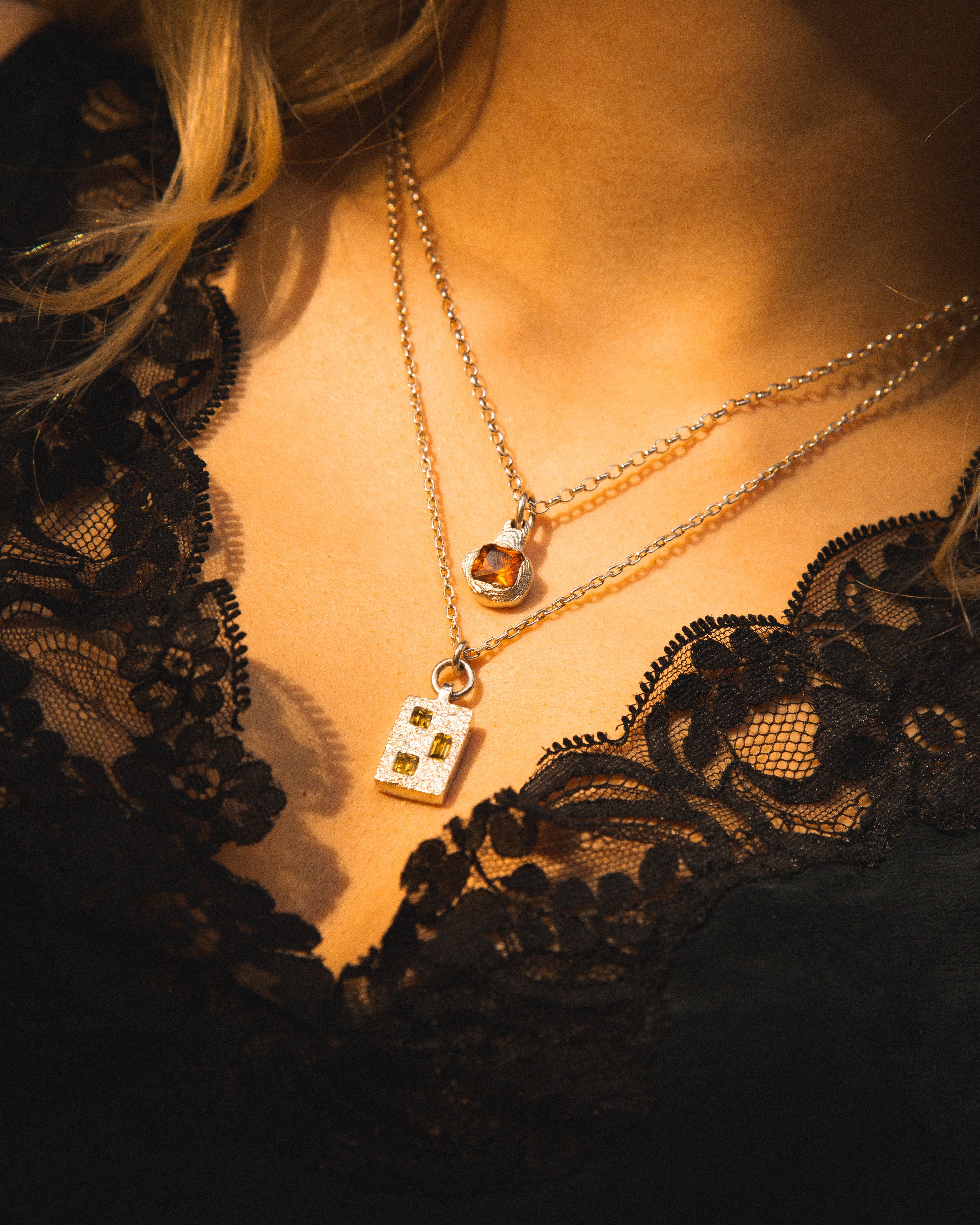 Close-up of a person wearing a gold necklace with a pendant, set against a dark lace garment.