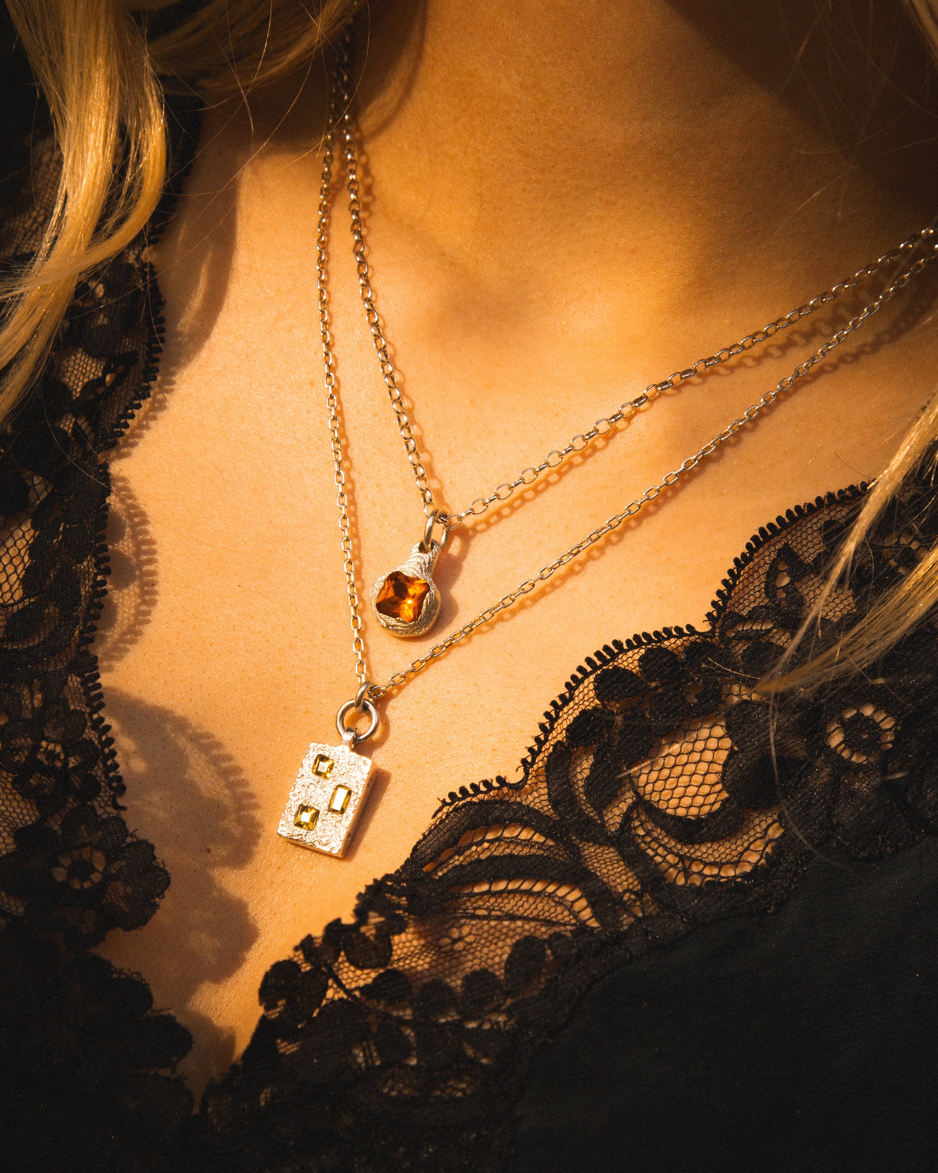 Close-up of a person wearing two necklaces with pendants on a dark background