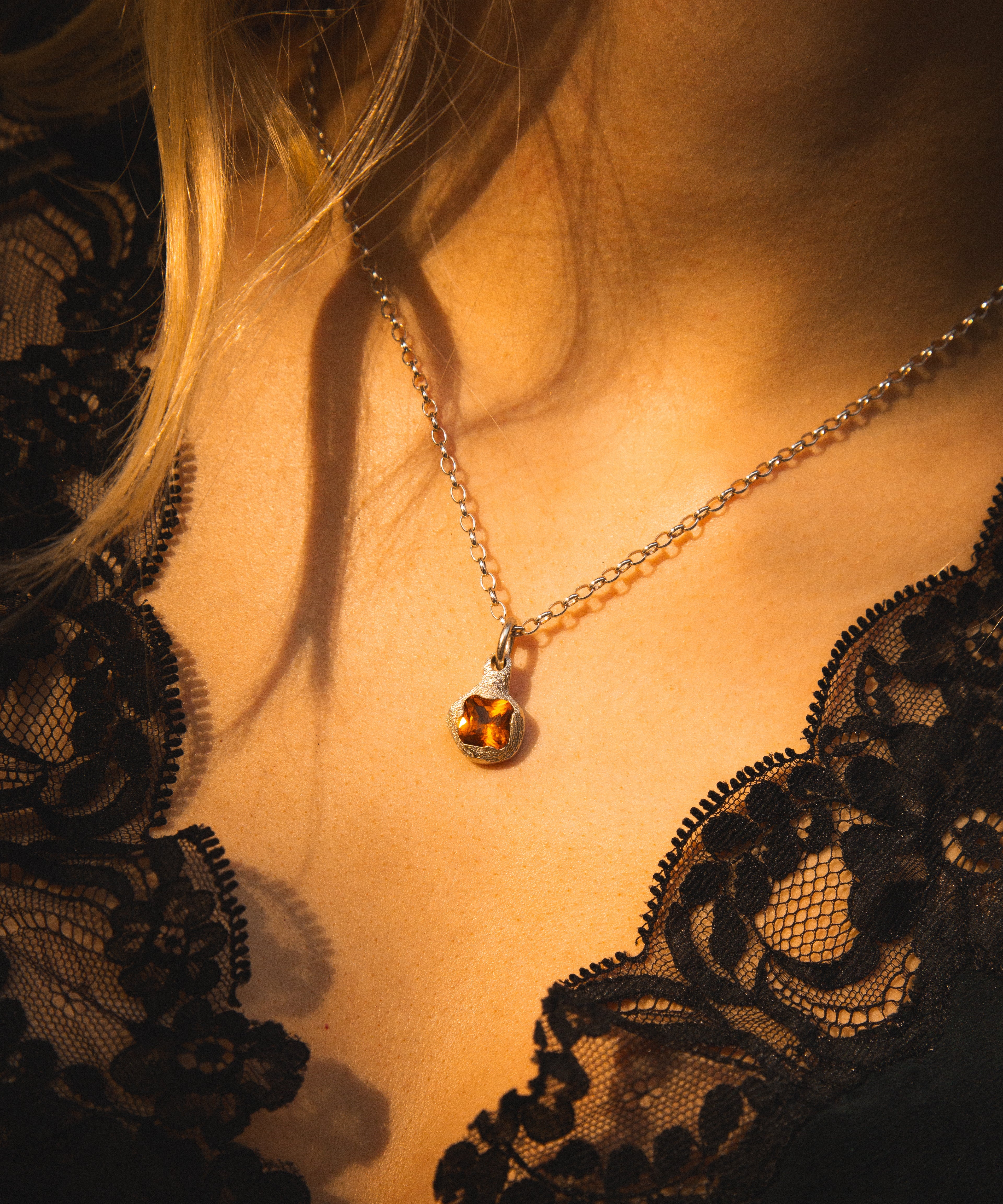 Close-up of a necklace with a pendant on a person wearing a black lace garment.