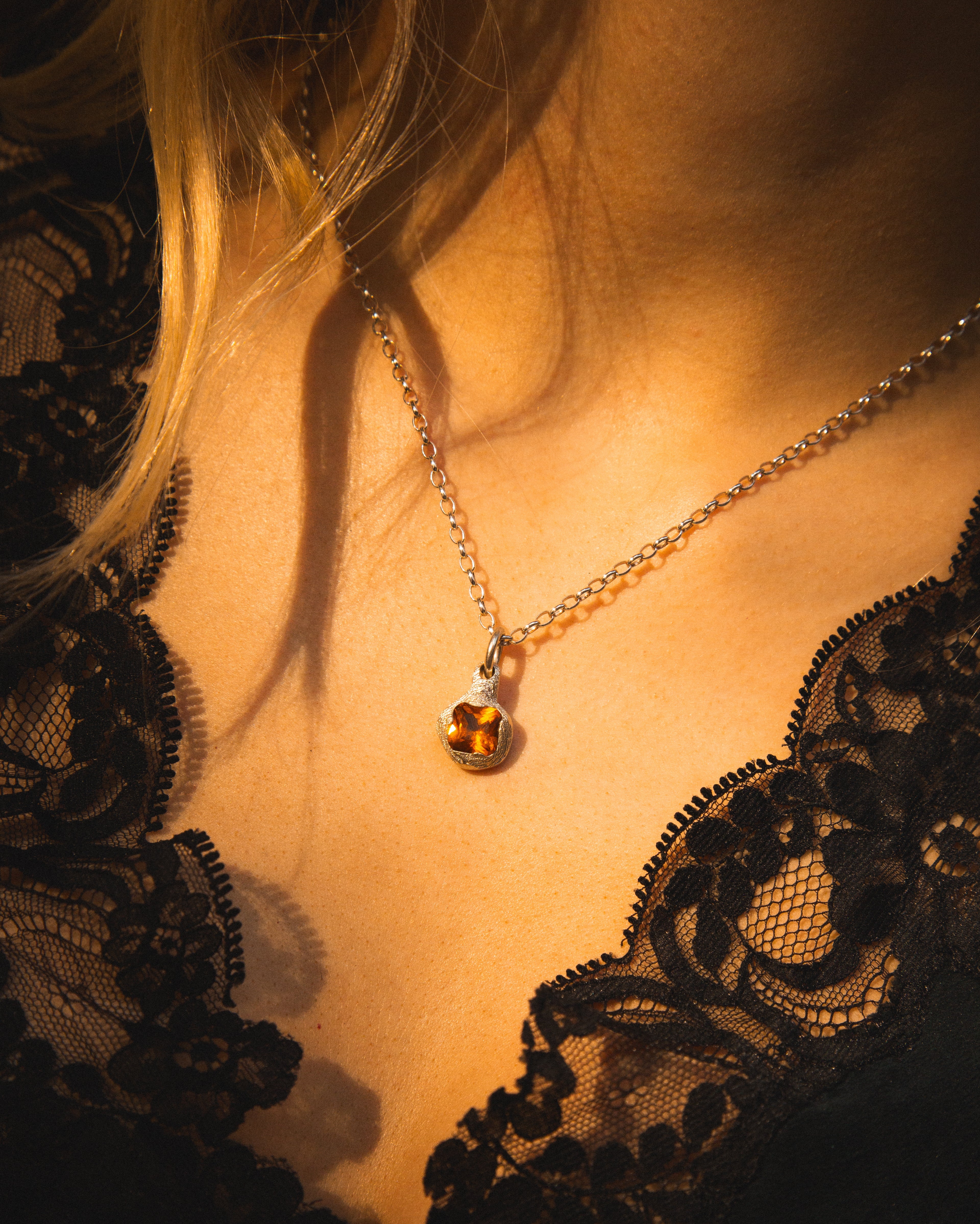 Close-up of a necklace with a pendant on a person wearing a black lace garment.