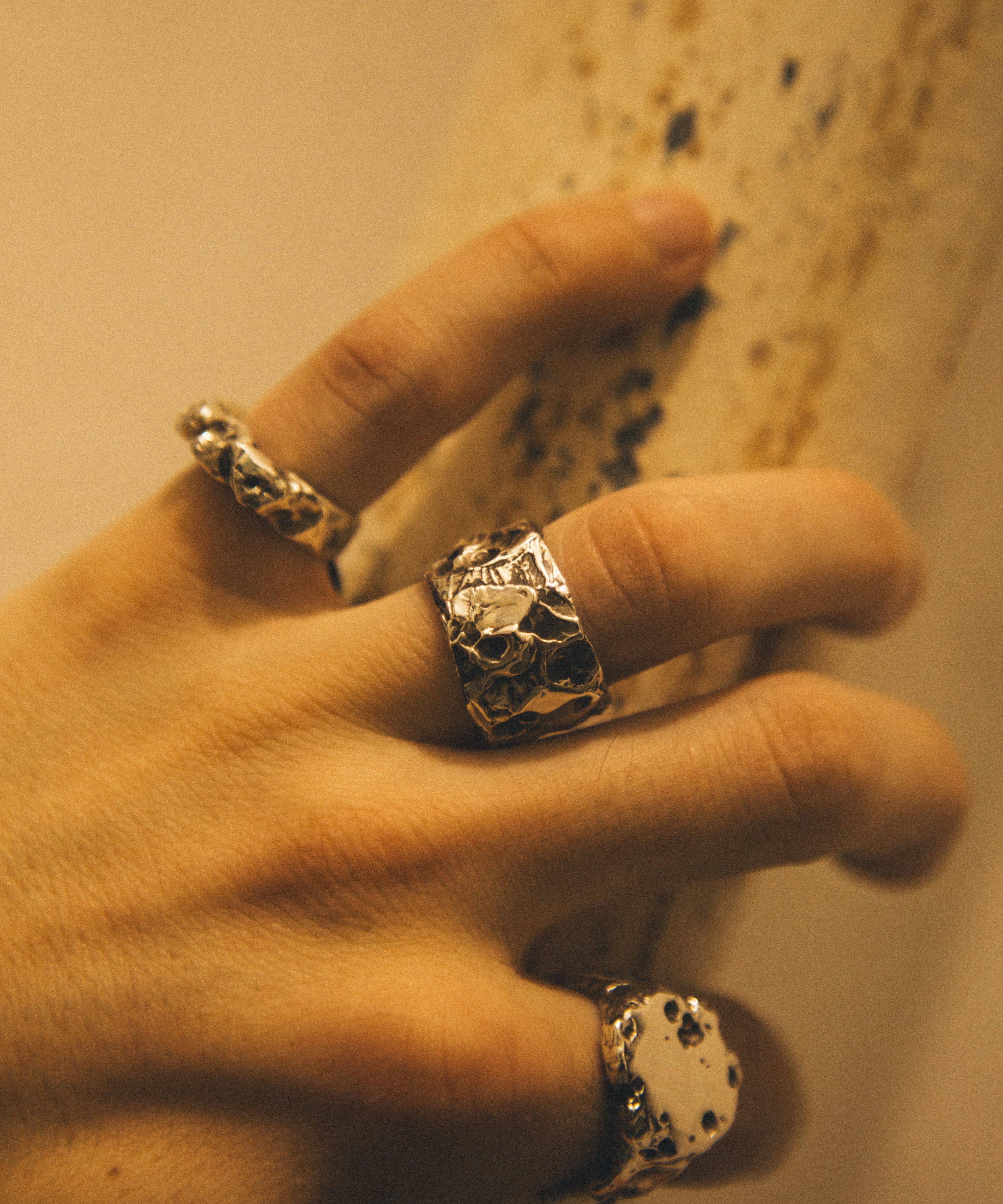 Hand wearing three metallic rings with a textured design on a neutral background