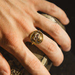 Hand wearing a gold ring with a gemstone on a textured surface