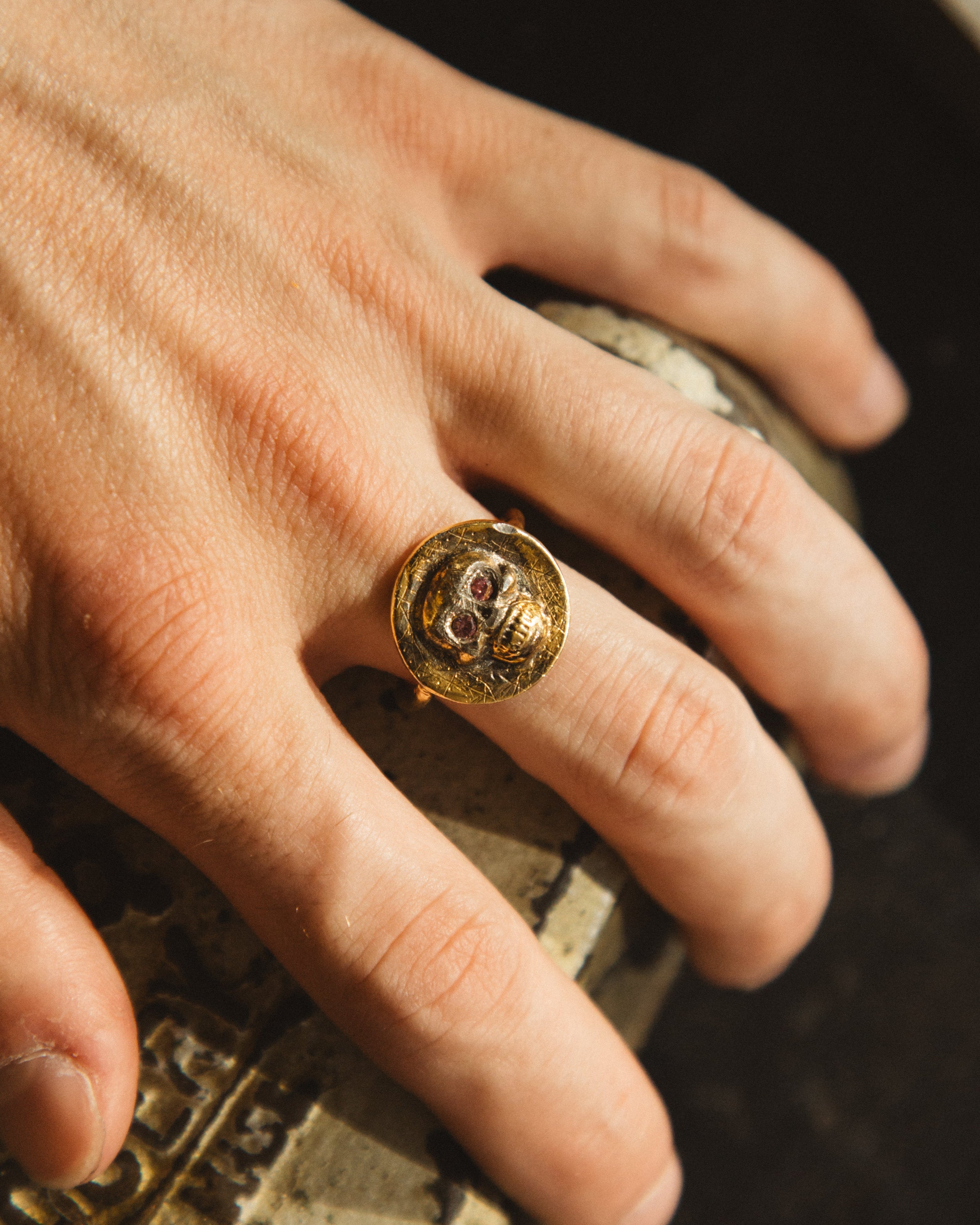 Hand wearing a gold ring with a gemstone on a textured surface