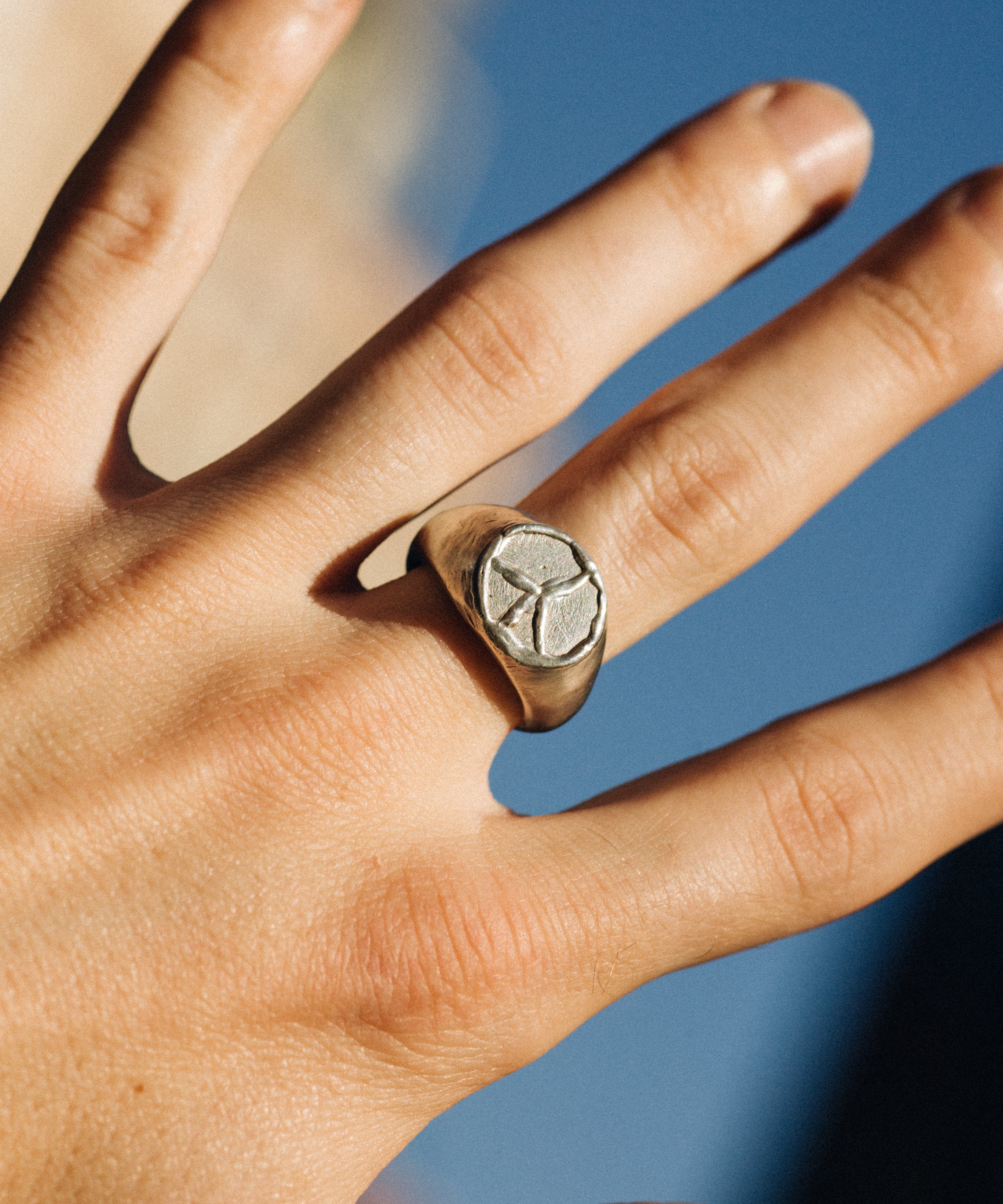 Hand wearing a silver ring with a stone against a blurred blue background