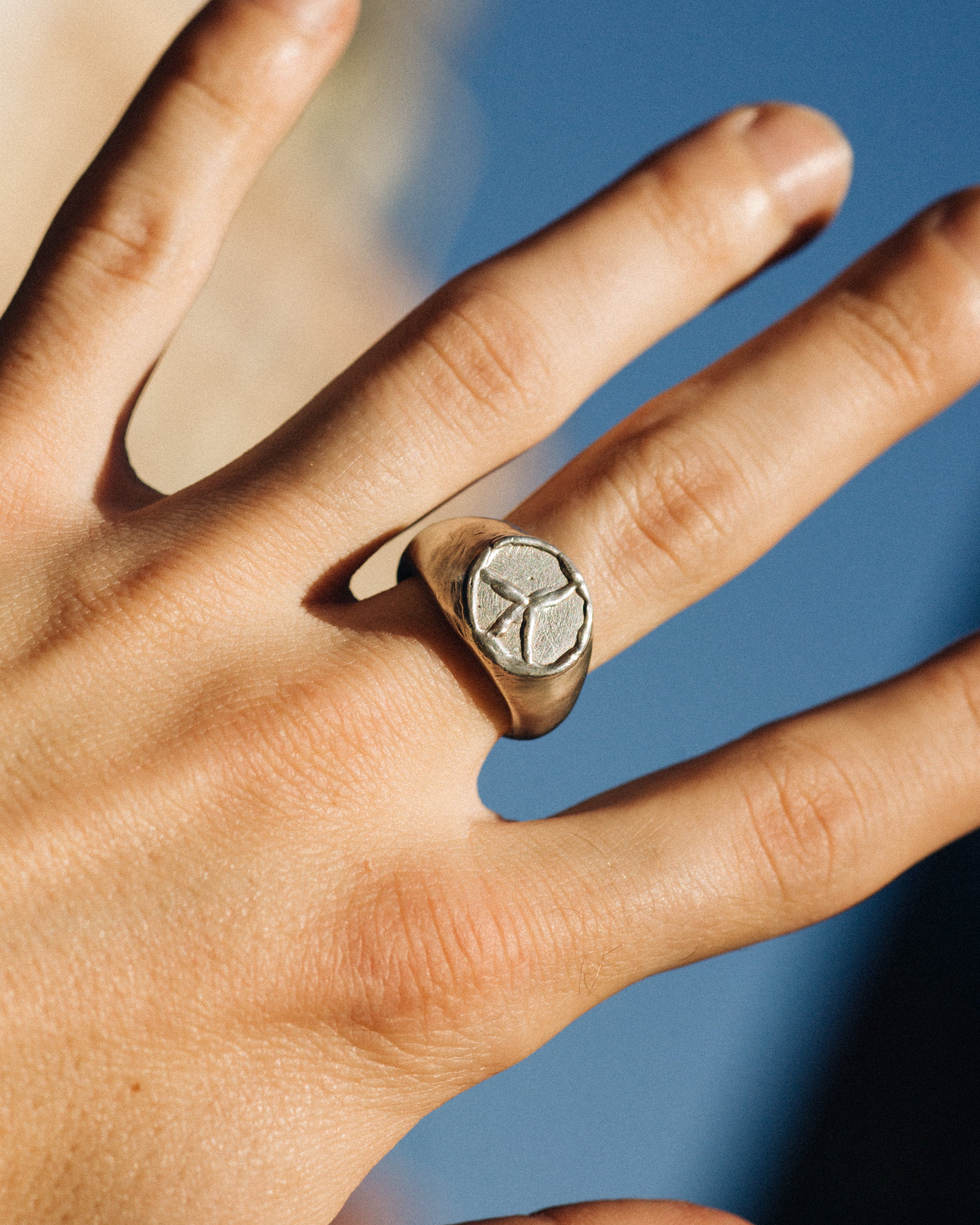 Hand wearing a silver ring with a stone against a blurred blue background