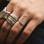 Close-up of a hand wearing multiple silver rings with tattoos on the fingers.