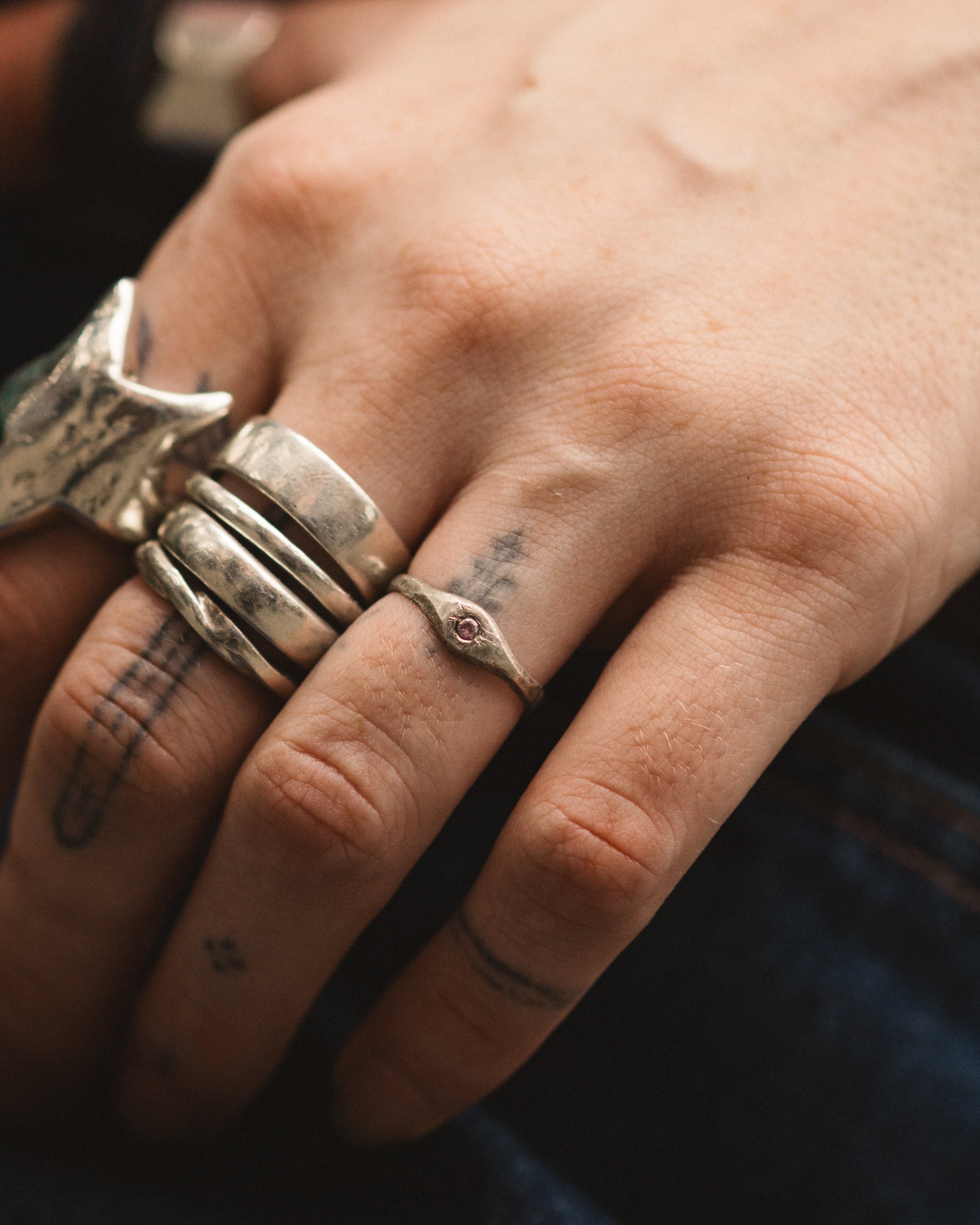 Close-up of a hand wearing multiple silver rings with tattoos on the fingers.