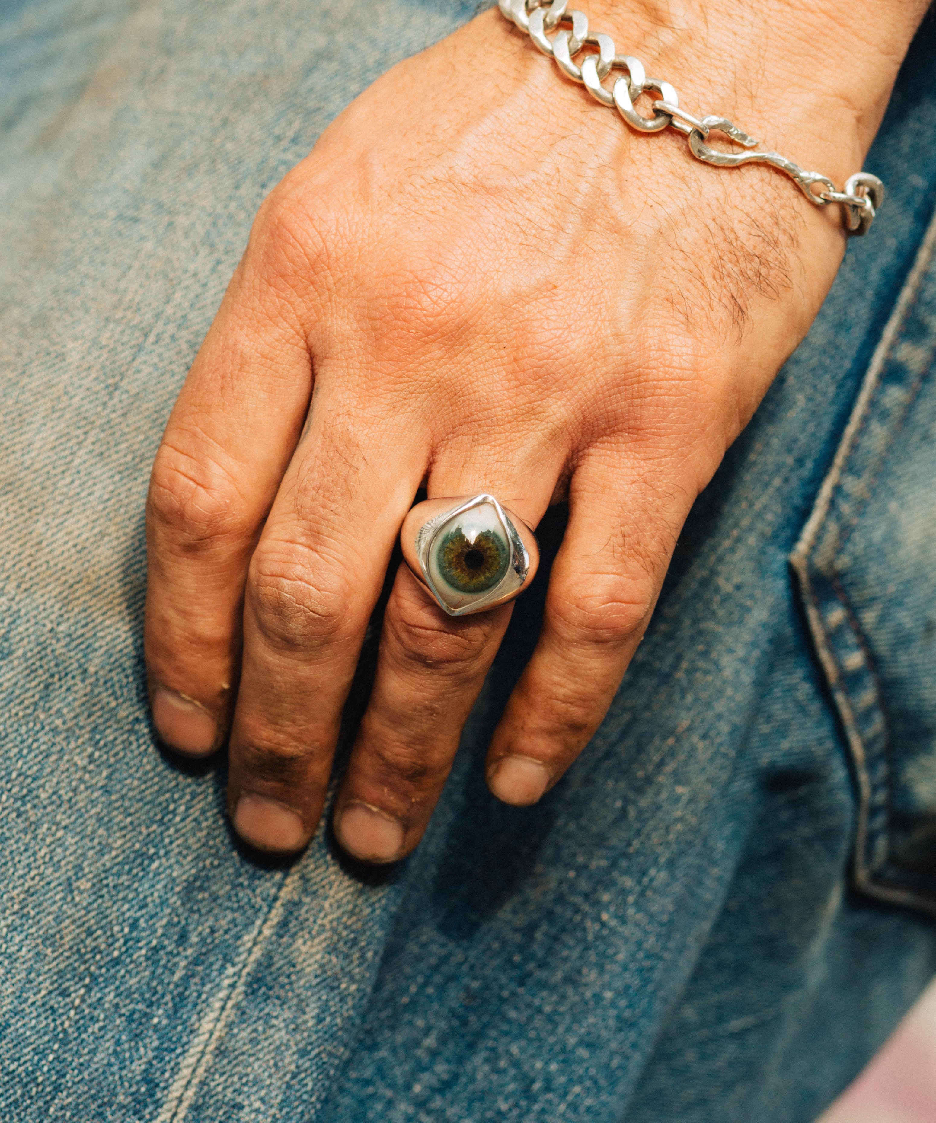 Hand wearing a ring and chain bracelet on denim fabric