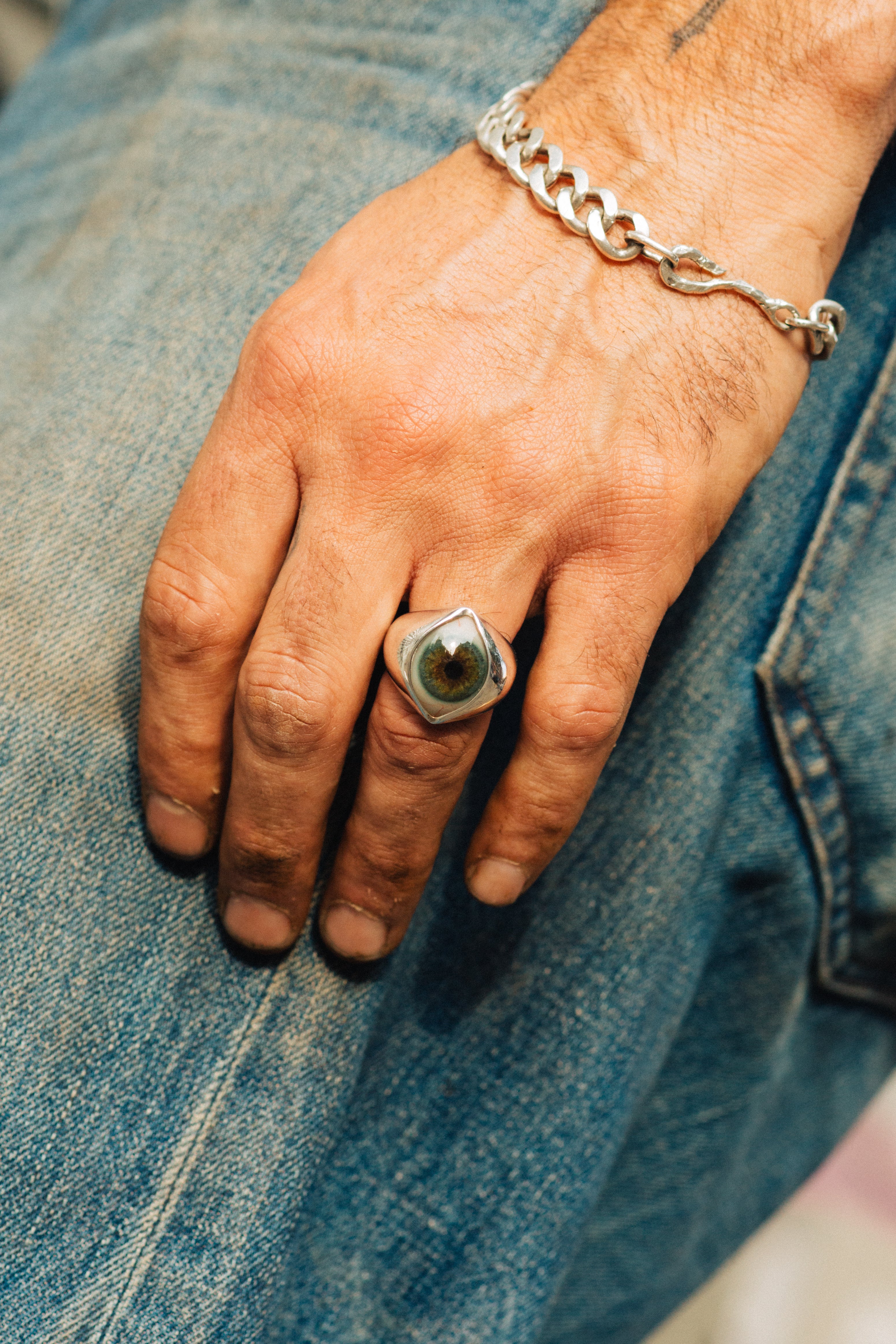 Hand wearing a ring and chain bracelet on denim fabric