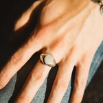 Hand wearing a ring with a stone, against a denim background