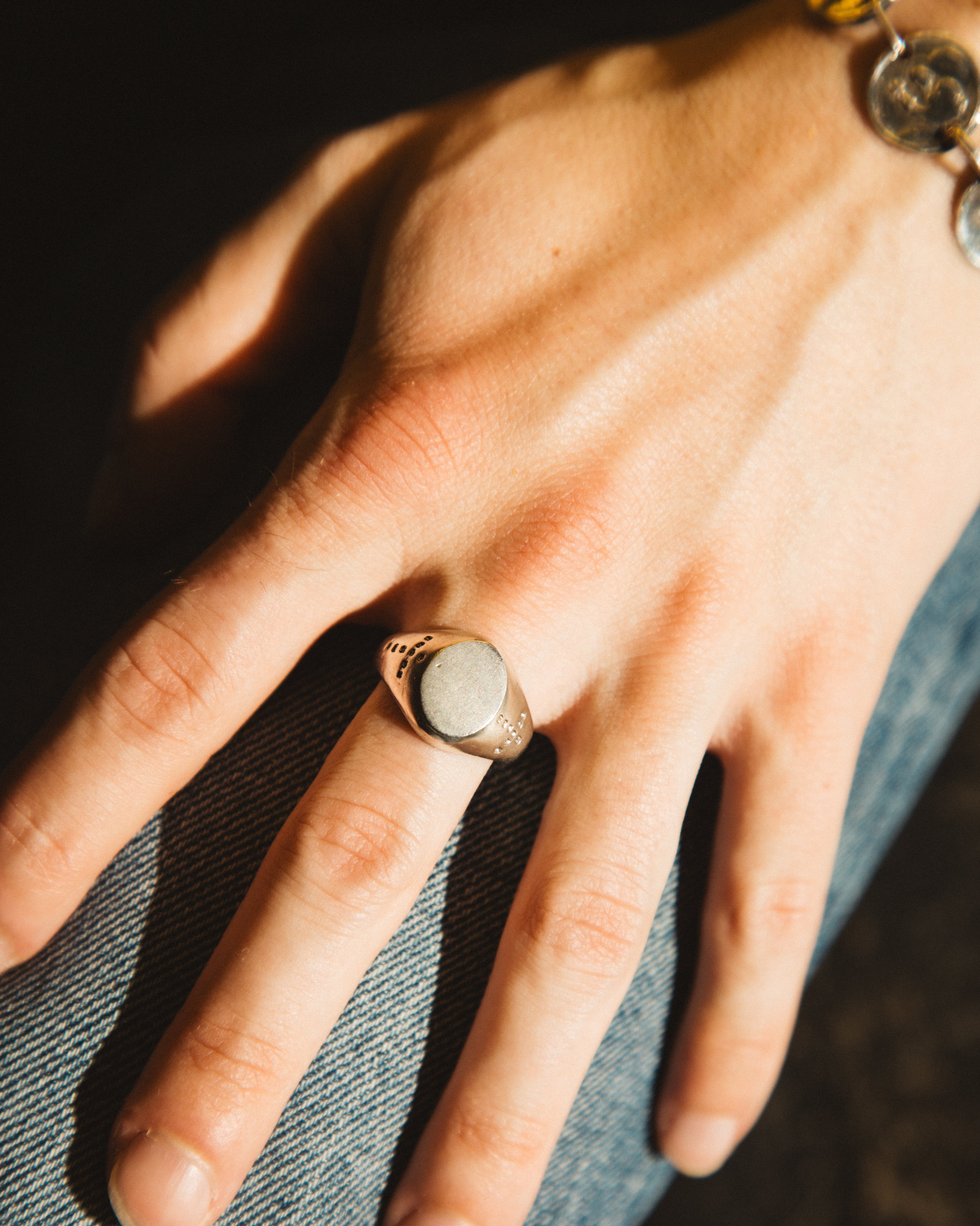 Hand wearing a ring with a stone, against a denim background