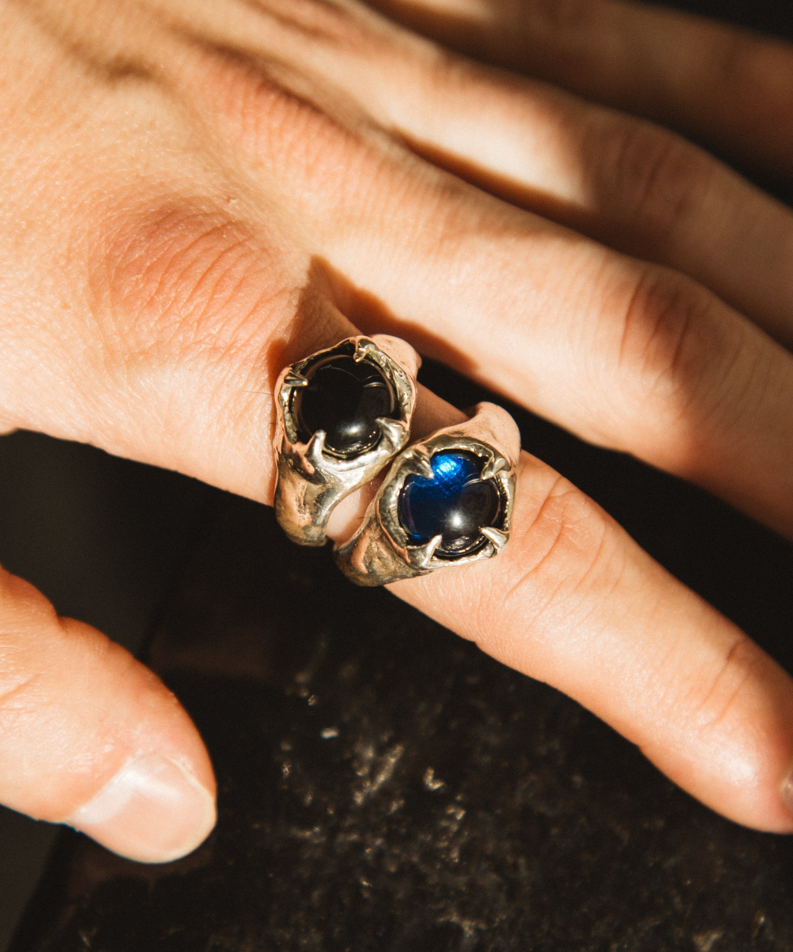 Close-up of a hand wearing two rings with gemstones on a dark background