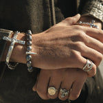 Close-up of a person's hands with multiple silver rings and bracelets on a dark background