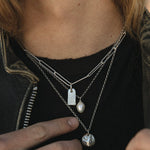 Person wearing multiple necklaces with pendants, focusing on the jewelry.